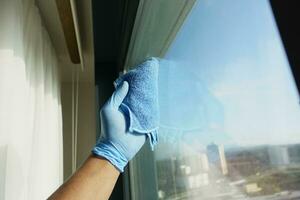 hand i blå handske rengöring fönster med blå trasa foto