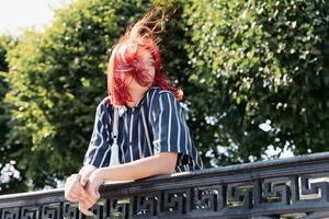 Tonårs flicka med röd hår gående i stad parkera, vind blåser, generation z foto