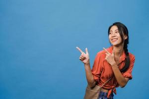 porträtt av ung asiatisk dam som ler med glatt uttryck, visar något fantastiskt på tomt utrymme i vardagskläder och står isolerat över blå bakgrund. ansiktsuttryck koncept.