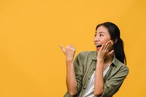 porträtt av ung asiatisk dam som ler med glatt uttryck, visar något fantastiskt på tomt utrymme i vardagskläder och står isolerat över gul bakgrund. ansiktsuttryck koncept. foto