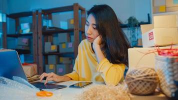 ung asiatisk affärskvinna tittar runt i rummet fullt av produktsaker och paketlåda känner sig stressad och upprörd med dålig försäljning på hemmakontoret på natten. småföretagare, online marknadsföringskoncept. foto