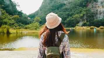 glad ung resenär asiatisk dam med ryggsäck som går vid fjällsjön. koreansk tonårsflicka njuta av sin semester äventyr känner glad frihet. livsstilsresor och koppla av i fritidskonceptet. foto