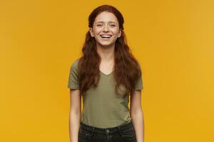 Lycklig skön ung kvinna med lång röd hår stående och skrattande isolerat över gul bakgrund ser på kamera foto
