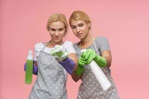 inomhus- Foto av ung vithuvud kvinnor med tillfällig frisyr innehav spray flaskor och svampar medan stående över rosa bakgrund i arbetssätt kläder