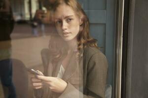 porträtt av ung ingefära kvinna ser genom fönster foto