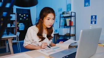 frilansande asiatiska kvinnor som använder laptop hårt arbete på nya vanliga hemmakontor. arbeta från huset överbelastning på natten, distansarbete, självisolering, social distansering, karantän för förebyggande av corona -virus.