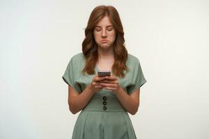 porträtt av upprörd ung Söt kvinna i årgång klänning med smartphones i händer, ser på skärm med ledsen ansikte, läsning dålig Nyheter, isolerat över vit bakgrund foto