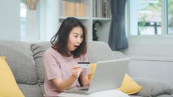 asiatisk kvinna som använder bärbar dator och kreditkort shopping e -handel, kvinnliga koppla av känner sig glad online shopping sitter på soffan i vardagsrummet hemma. livsstil kvinnor slappna av hemma koncept. foto