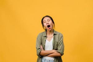 porträtt av ung asiatisk dam med negativt uttryck, uttråkad gäspande trött täckande mun med handen i vardagskläder isolerad på gul bakgrund med tomt kopieringsutrymme. ansiktsuttryck koncept