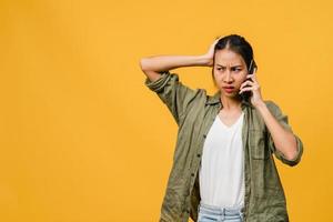 ung asiatisk dam pratar i telefon med negativt uttryck, upphetsad skrik, gråter känslomässigt arg i avslappnad trasa och står isolerad på gul bakgrund med tomt kopieringsutrymme. ansiktsuttryck koncept.