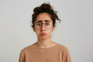 porträtt av olycklig besviken georgiansk ung kvinna med lockigt hår bär beige pullover och glasögon känner ledsen och deprimerad isolerat över vit bakgrund foto
