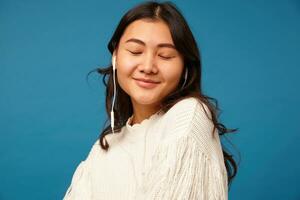 horisontell Foto av ung härlig lång håriga asiatisk lady med naturlig smink lyssnande till musik och leende försiktigt med stängd ögon, isolerat över blå bakgrund