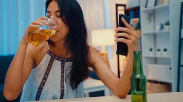 ung asiatisk dam som dricker öl som har roligt lyckligt ögonblick nattfest nyårshändelse online firande via videosamtal via telefon hemma på natten. social distansering, karantän för förebyggande av coronavirus.