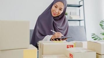 ung asien muslimsk affärskvinna kontrollera produkt inköpsorder på lager och spara till surfplatta arbete på hemmakontor. småföretagare, onlinemarknadsleverans, livsstil frilansande koncept.
