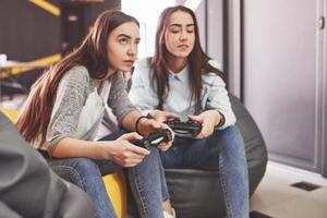 tvillingsyster systrar spelar på konsolen. tjejer håller joysticks i händerna och har kul