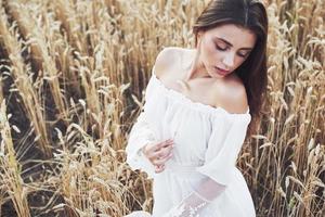 ung känslig tjej i vit klänning poserar i ett fält av gyllene vete foto