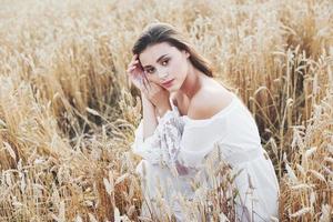ung känslig tjej i vit klänning poserar i ett fält av gyllene vete foto