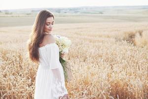 vacker flicka i vit klänning som körs på höstfältet av vete vid solnedgången