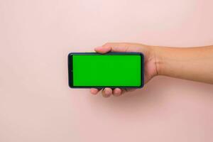mänsklig hand innehav mobil smartphone med grön skärm i horisontell placera isolerat på rosa bakgrund. foto