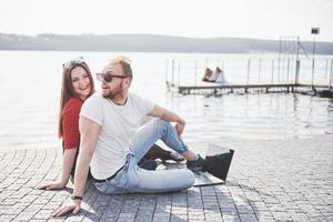 två studenter kille och flicka sitter utomhus och njuter av en bärbar dator, studerar utomhus på en solig dag foto