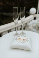 guld bröllop ringar på en kudde dekorerad i en cirkel med silver- Smycken stenar, bröllop glasögon närliggande, förberedelse för de målning ceremoni foto