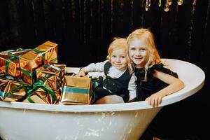 glad jul och Lycklig högtider. glad flicka och pojke i en bad med jul gåvor i guld omslag. barn är har roligt. kärleksfull familj med gåvor i de rum. foto