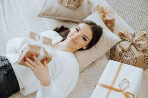 en skön och eleganta ung flicka i en vit Tröja lögner på de golv av henne rum mellan jul presenterar i ny år lampor foto