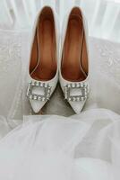 vit kvinnors skor med swarovski stenar, stående på en stol, Nästa till de brudens slöja. närbild Foto