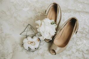 detaljer av de brudens kläder. guld bröllop ringar i en glas dekorativ låda stående på bomull blommor. bröllop blomma av de brudgum. kvinnors högklackade skor av gyllene Färg foto