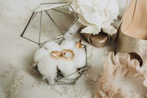 detaljer av de brudens kläder. guld bröllop ringar i en glas dekorativ låda stående på bomull blommor. bröllop blomma av de brudgum. kvinnors högklackade skor av gyllene Färg foto