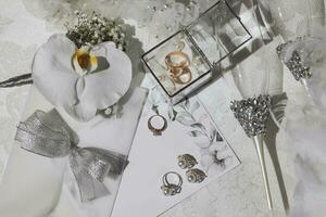 bröllop detaljer i silver- Färg på en vit bakgrund. bröllop ringar och örhängen med pärlor, glasögon på silver- står. guld bröllop ringar i en glas låda. foto