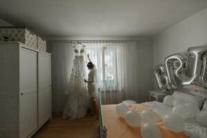en skön ung brud i en vit underkjol är stående förbi de fönster, rörande henne bröllop klänning. slutlig förberedelser för de bröllop. de brud är väntar för de brudgum. morgon, brud. foto