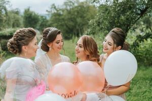 de brudtärnor se på de leende brud. de brud och henne roligt vänner fira en bachelorette fest utomhus i matchande klänningar. de brud och vänner på de gräs under de öppen himmel foto