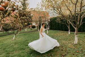 söt brud i vit klänning med lång tåg, brud cirkulerande i trädgård, skog utomhus. bröllop fotografi, porträtt av en leende brud. foto