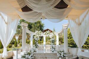 de bröllop ceremoni är dekorerad med färsk blommor på de plats med lång vit kolumner. förberedelse för de bröllop ceremoni foto