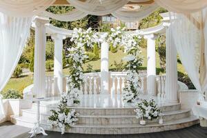 de bröllop ceremoni är dekorerad med färsk blommor på de plats med lång vit kolumner. förberedelse för de bröllop ceremoni foto