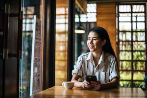 kvinna sitter och spelar sin smarta telefon på café foto