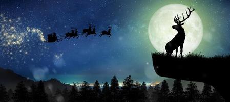 silhuett av renar som står på klippan för att se jultomten flyga på sina renar över fullmånen på natten jul. foto