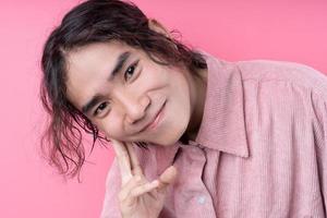 långhårig ung asiatisk man, iklädd rosa skjorta, leende på rosa bakgrund foto