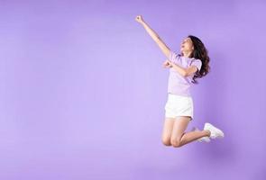 ung asiatisk tjej som hoppar upp på lila bakgrund