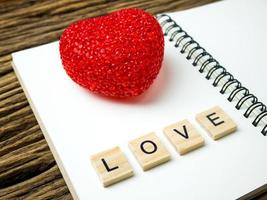 ovanifrån av anteckningsbok med rött hjärta på trä svart bakgrund, kärleksord i träkub foto