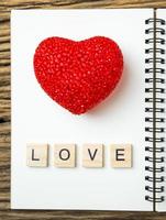 ovanifrån av anteckningsbok med rött hjärta på trä svart bakgrund, kärleksord i träkub foto