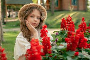 drömmande mellan flicka Framställ nära rabatt med blomning röd salvia i trädgård foto