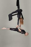 skön flicka och ett atletisk man i en svart sport kostymer är utför ett akrobatisk element i en studio. foto