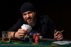 skäggig man med cigarr och glas Sammanträde på poker tabell och skrikande isolerat på svart foto