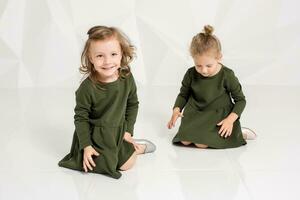 två liten flick i de samma mörk grön klänningar Sammanträde på de golv i en studio med vit väggar foto