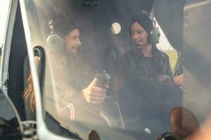 två Lycklig tonåring flickor i pilot headsets talande i helikopter cockpit foto