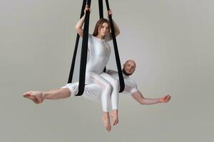 skön flicka och ett atletisk man i en vit sport kostymer är utför ett akrobatisk element i en studio. foto
