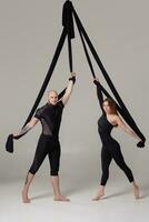 skön flicka och ett atletisk man i en svart sport kostymer är utför ett akrobatisk element i en studio. foto