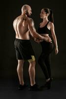 atletisk man i shorts och gymnastikskor med brunett kvinna i damasker och topp Framställ på svart bakgrund. kondition par, Gym begrepp. foto